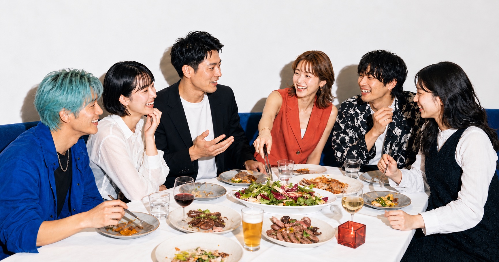 白い壁と青いソファのあるレストランで、食事とお酒を楽しむ男女6人